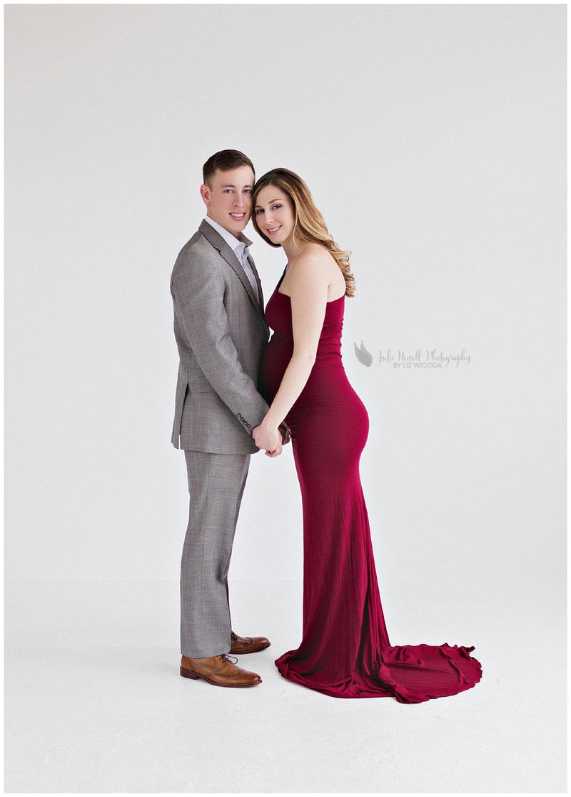 Pregnant mother wearing the Anita gown in wine by Sew Trendy standing with husband in studio.