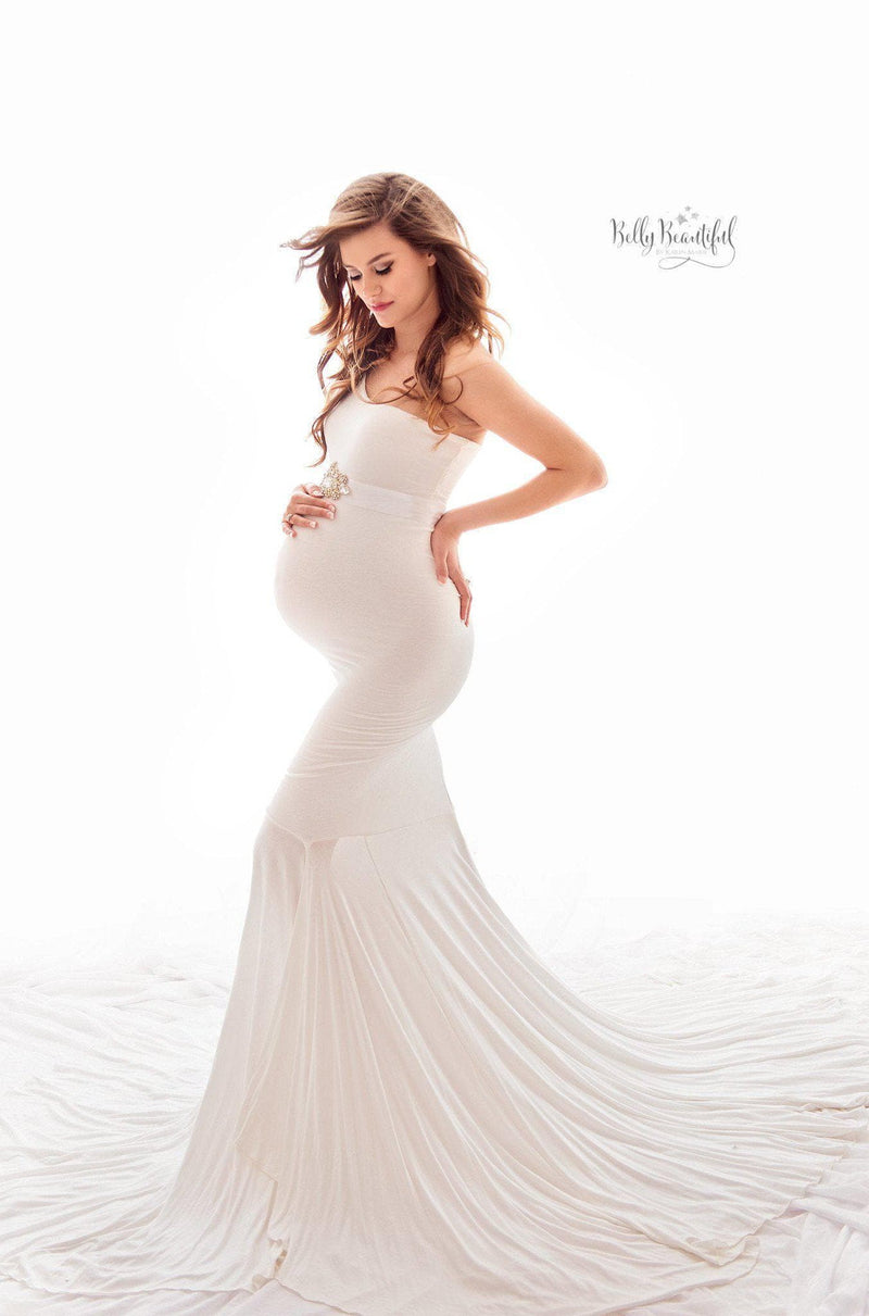 Pregnant woman wearing the Bonnie gown in white by Sew Trendy, standing in studio on white backdrop.