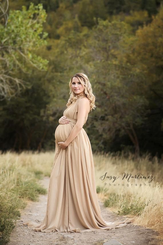 Pregnant woman wearing the Carolynne gown in Camel by Sew Trendy standing on forest path