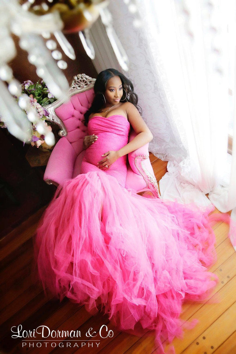 Pregnant woman wearing Celine gown in fuchsia by Sew Trendy sitting in pink chair by window with chandelier above