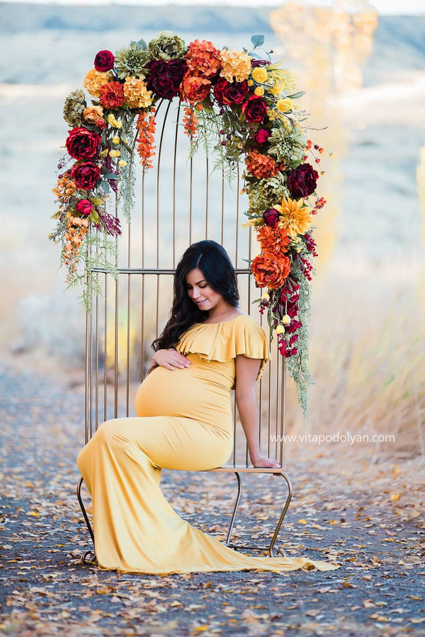 Expecting mother wearing the Colbie gown in gold by Sew Trendy sitting in floral chair in autumn