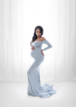 Pregnant woman wearing the Emerlie gown in blue rain by Sew Trendy standing in backlit studio