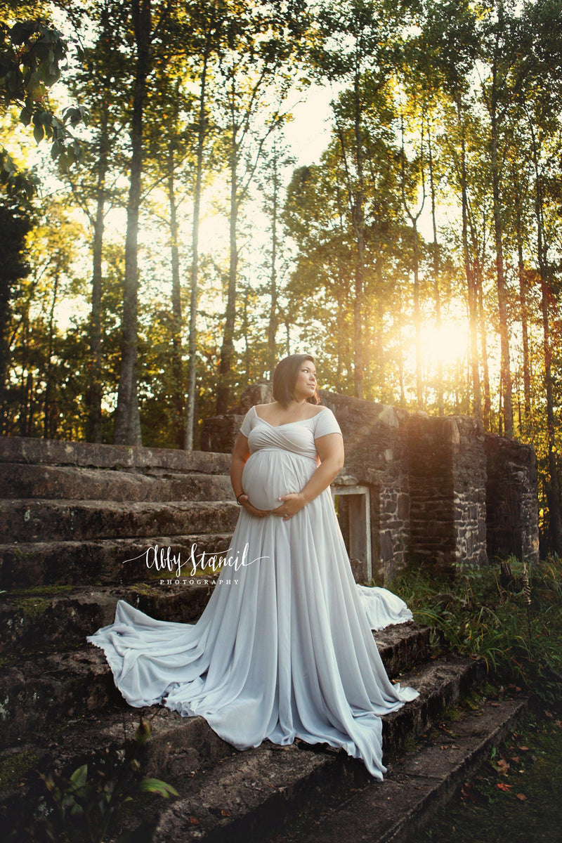 Expecting mother wearing the Faythe gown in grey by Sew Trendy standing on old stone stairs at sunset