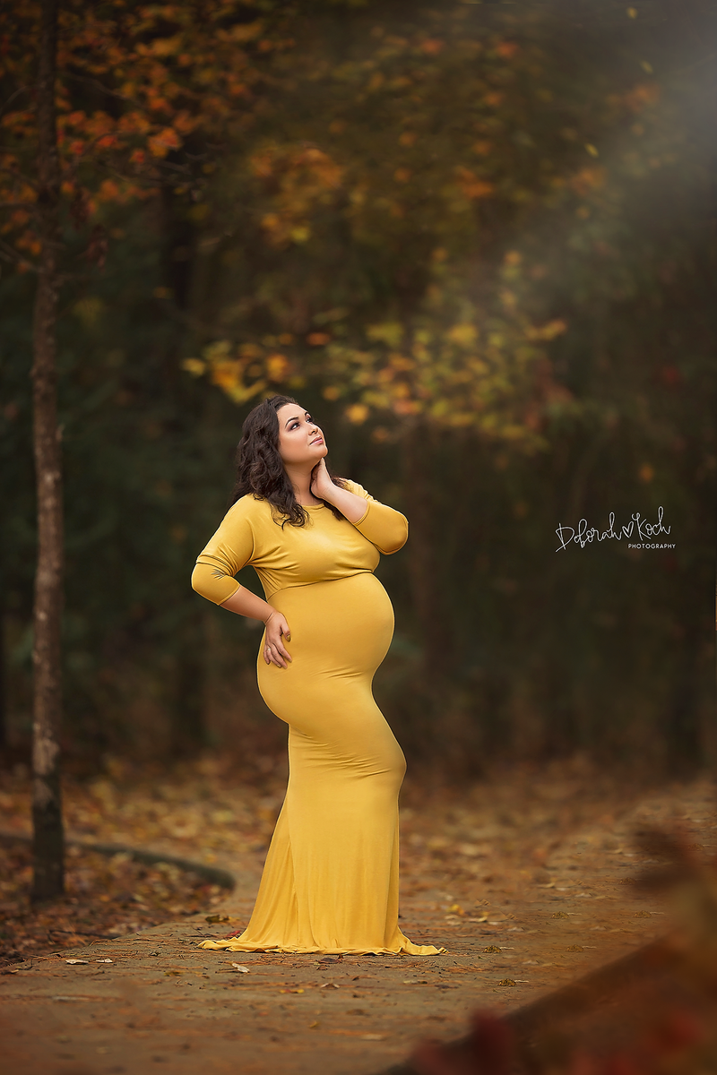 Pregnant mother in the Jaden Gown in Gold by Sew Trendy Accessories on a bridge in the forest.