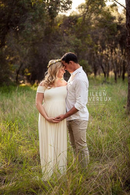Pregnant mother in the Kelly Gown by Sew Trendy Accessories in Ivory with trees and grass.