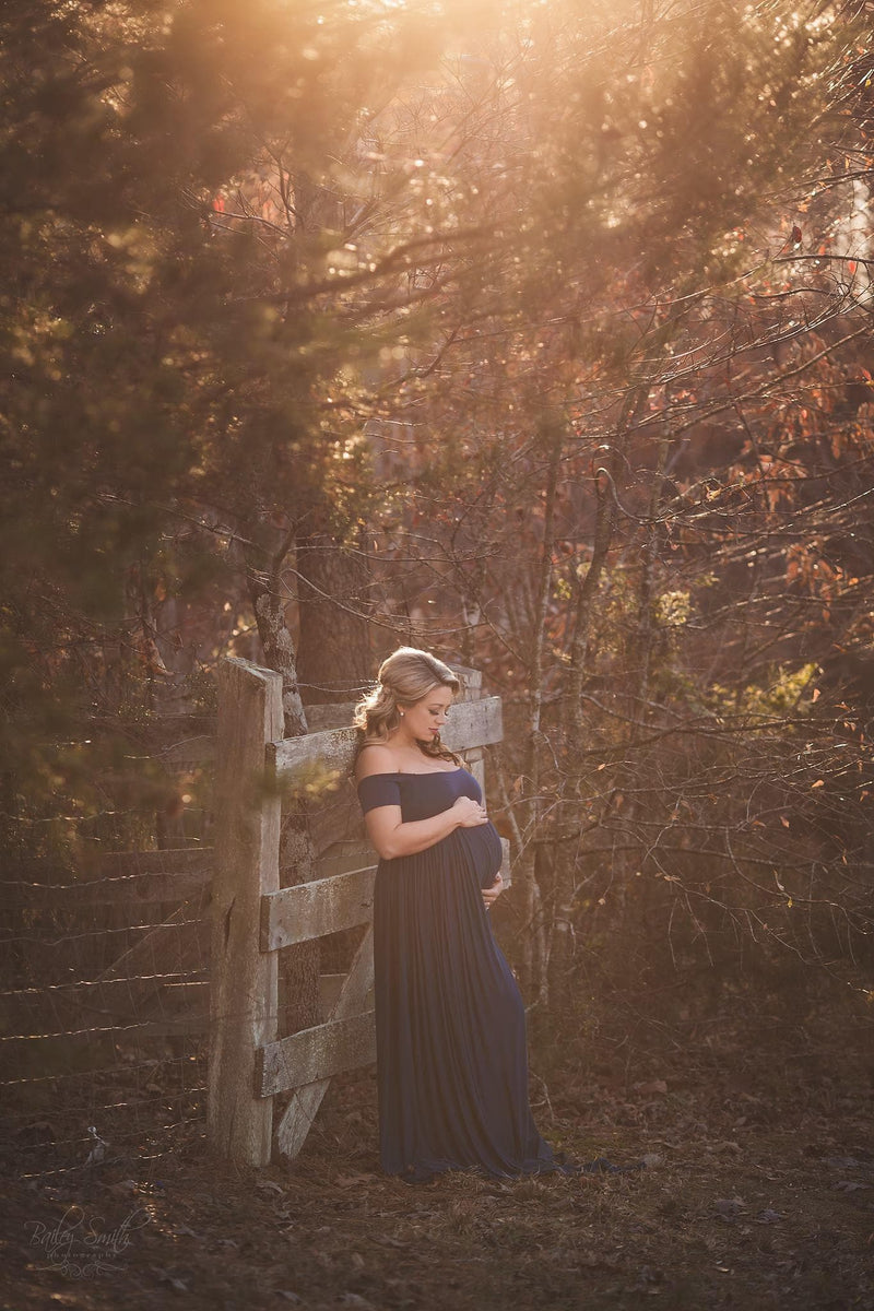 Pregnant mother in the Kelly Gown by Sew Trendy Accessories with a fence and trees.