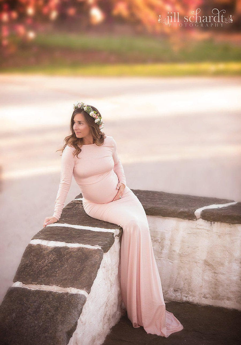 Pregnant mother in the Krysten Gown by Sew Trendy Accessories in Blush with a flower crown sitting on a wall.