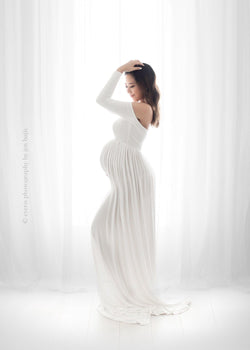 Pregnant woman in the Miriam Gown in White by Sew Trendy Accessories in the studio with a white background.