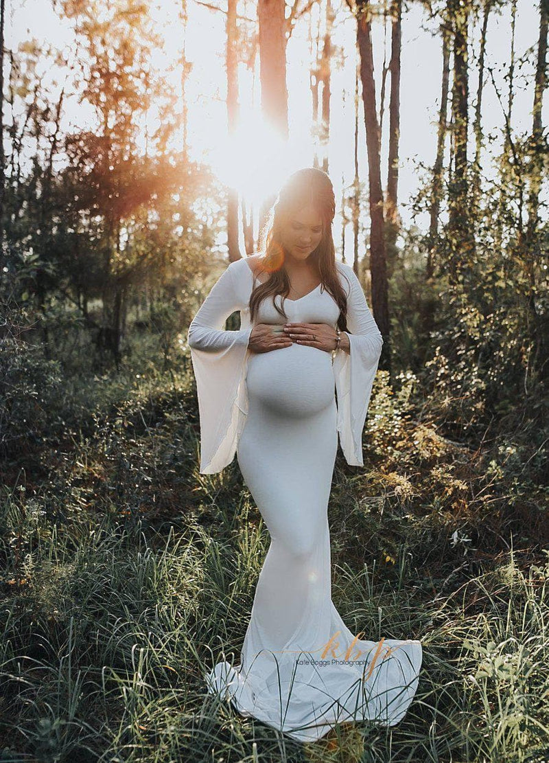 Expecting mother wearing Vanae gown in ivory by Sew Trendy standing in forest