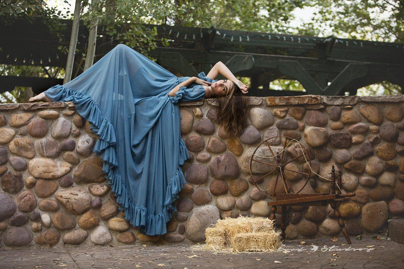 Model in the Paulina Gown in Blue Steel by Sew Trendy Accessories standing laying on a brick wall.
